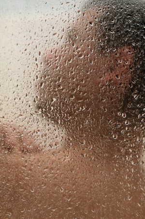 A man scrubbing his shoulders though the shower door. Water drops are in focus.